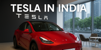Tesla in India: Model Y Price, Specs & Launch – Everything You Need to Know Red Tesla Model Y displayed in a modern Tesla showroom in India with “Tesla in India” signage and large glass windows overlooking an urban skyline.